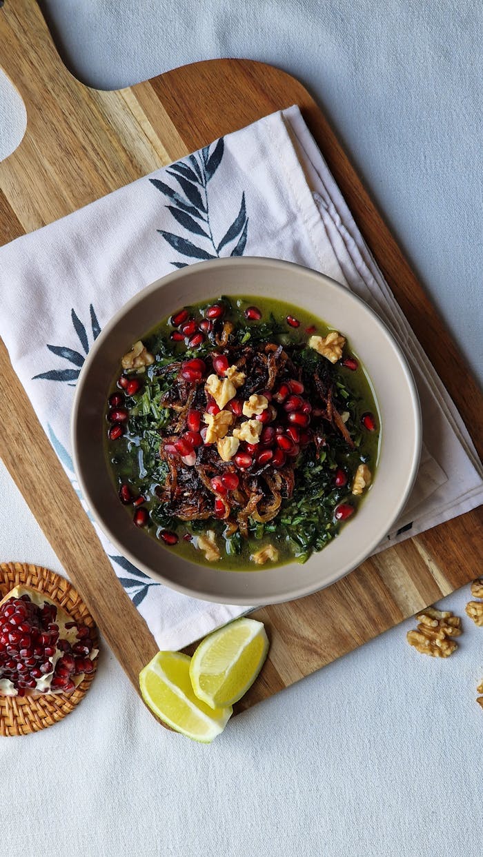 hero-img-01 A healthy kale salad topped with pomegranate seeds, walnuts, and lemon slices on a wooden board.