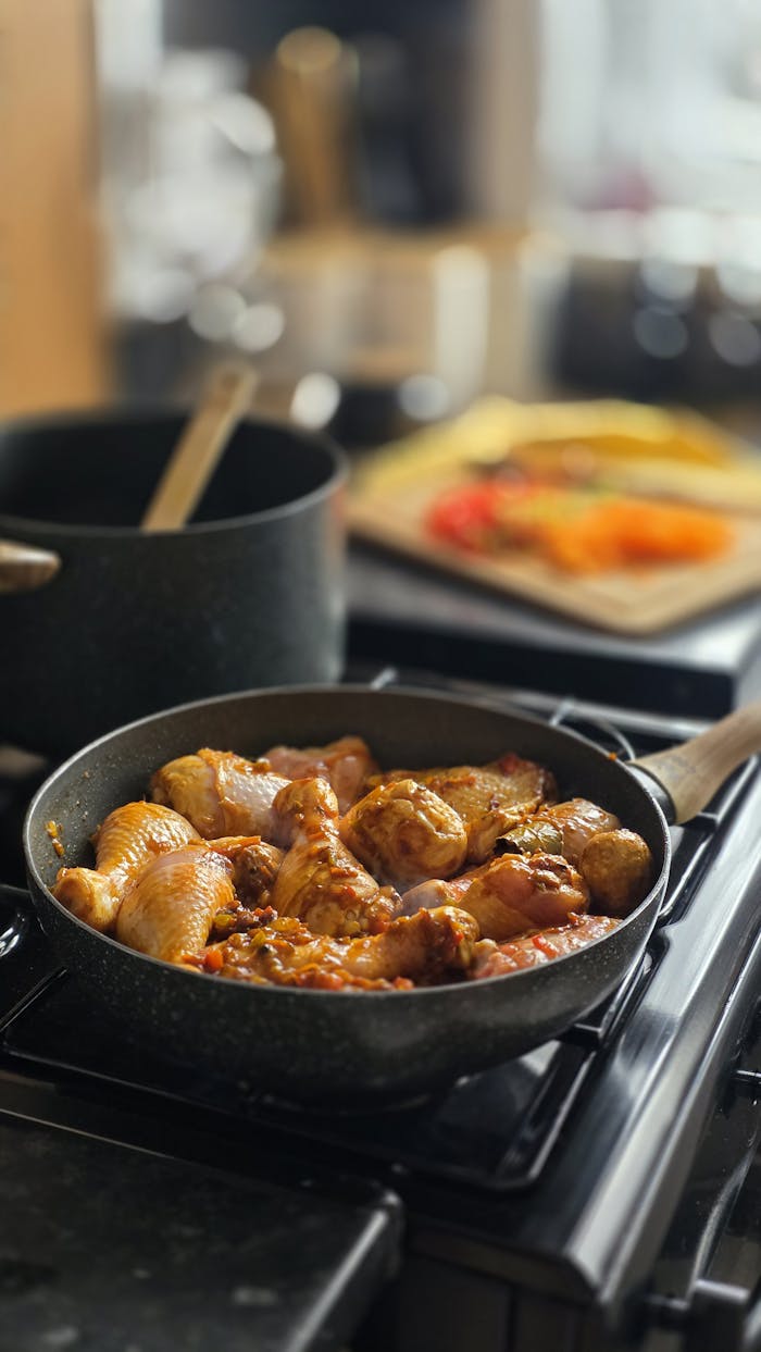 gallery-4 Juicy chicken pieces cooking in a frying pan with herbs and spices, creating a savory meal.