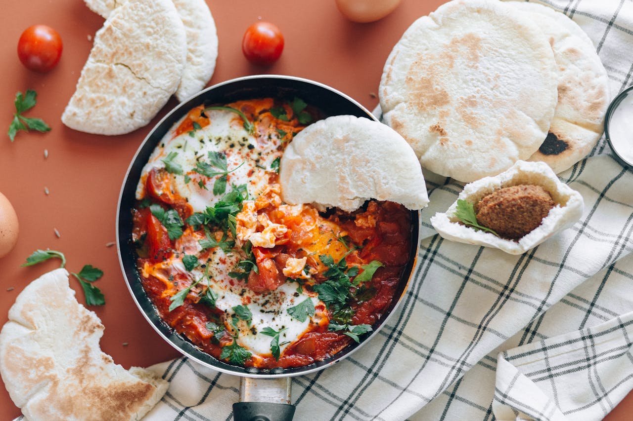 why-choose-us Top view of shakshuka meal with pita bread, cherry tomatoes, and fresh herbs.