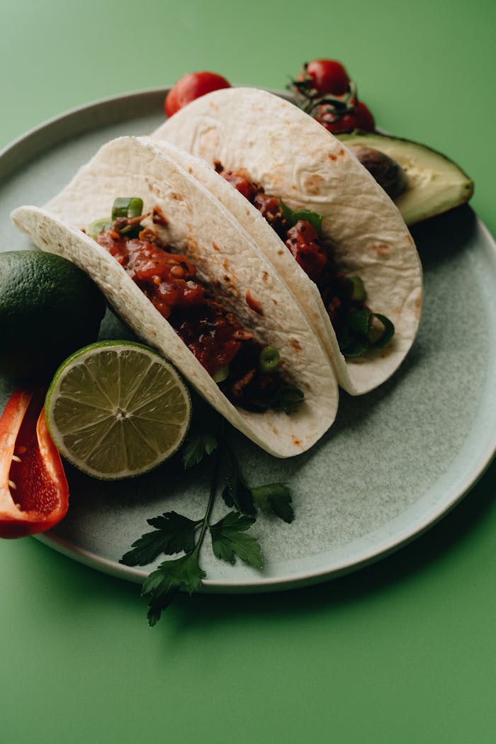 gallery-5 Delicious tacos with fresh avocado, lime, and peppers on a plate.