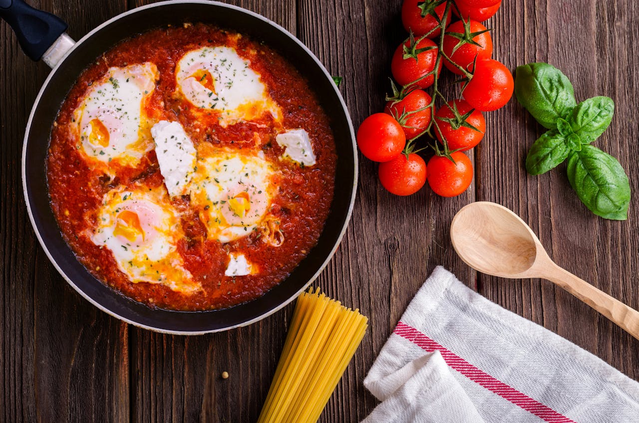 services-03 Delicious eggs in tomato sauce with basil, spaghetti, and fresh tomatoes on a wooden table.